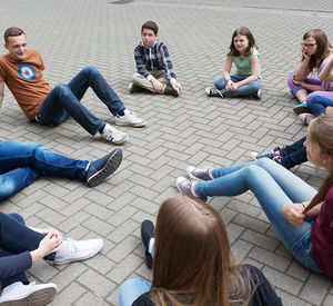 Jugendliche sitzen im Kreis auf dem Schulhof.